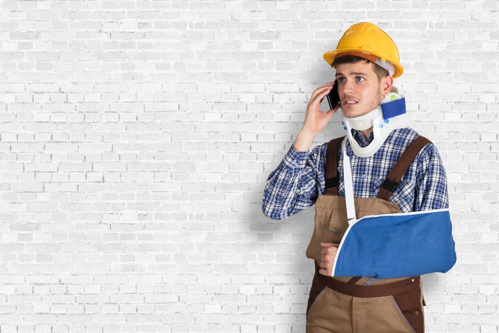 Injured construction worker in neck brace and arm sling talking on phone – working while on workers’ compensation in Greensboro
