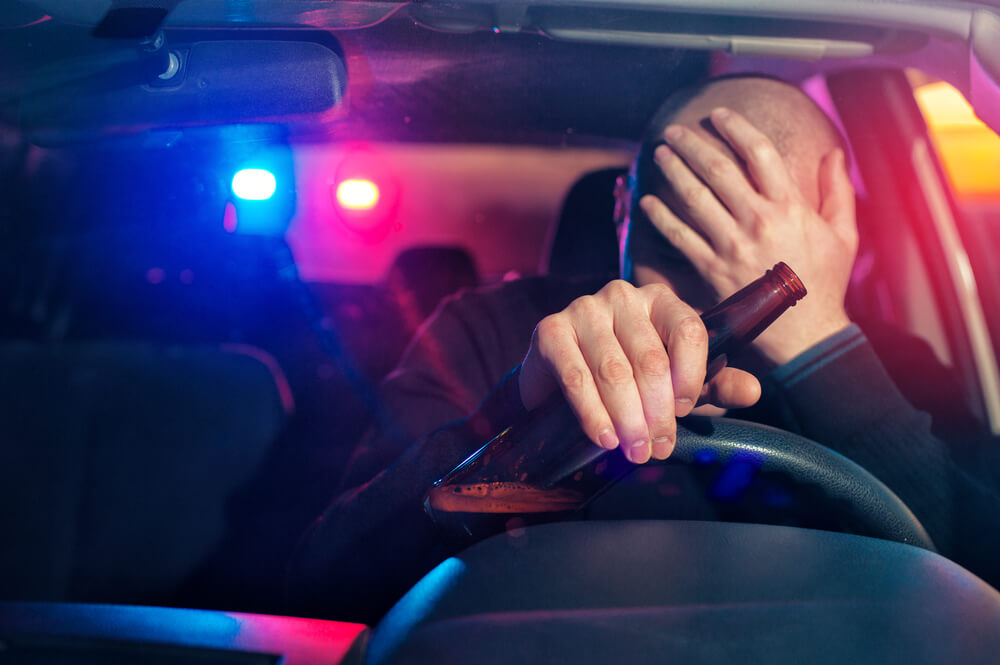 Drunk driver stopped by police in North Carolina with beer bottle in hand – concept of DUI accident and legal consequences.