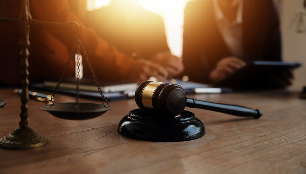 Gavel and scales of justice on desk with Greensboro personal injury attorneys discussing a case in the background.