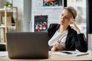 Stressed professional woman at desk struggling with PTSD symptoms after a workplace incident, considering workers’ compensation claim.